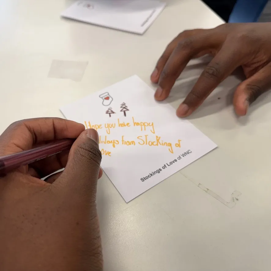 A student’s hands writing a Stockings of Love notecard