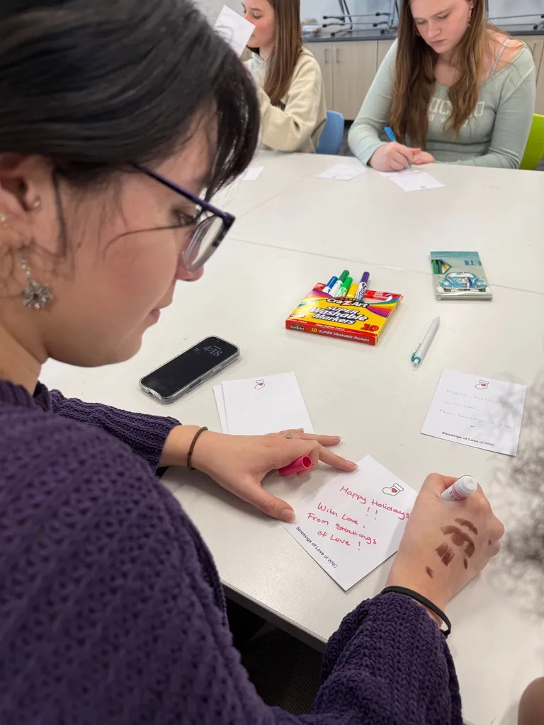A student writing a holiday notecard with markers