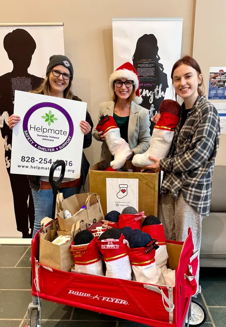 Three women with a Helpmate sign and a red wagon full of stockings